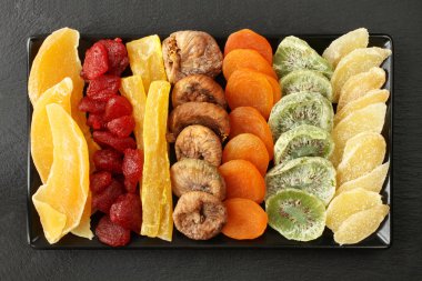 Mango, papaya, kivi, Kuru Meyve parçaları; kurutulmuş çilek, incir, kayısı; adet siyah seramik tabak siyah bir taş yüzey içinde yatan şekerlenmiş zencefil kökü. Makro