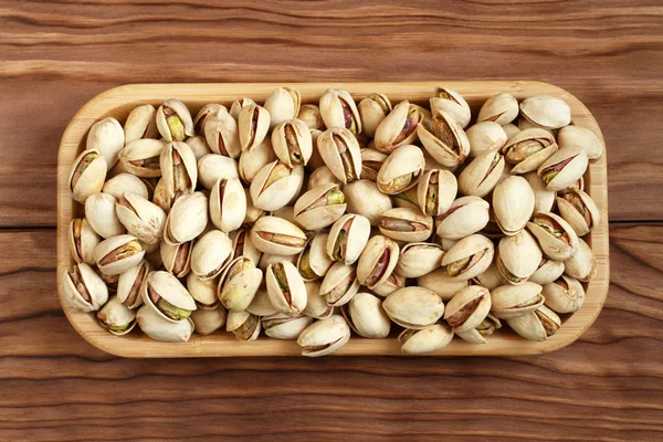 Salted dried pistachio nuts in bamboo plate on wooden background. View from above — Stock Photo, Image