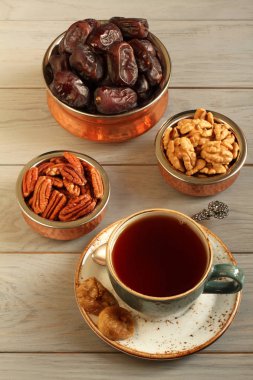 Vejetaryen tatlı: bakır kaselerde kurutulmuş hurma, pekan ve ceviz, bir tabak ve gri ahşap masada siyah çay bir fincan kuru incir. Closeup