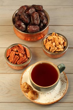 Vejetaryen tatlı: bakır kaselerde kurutulmuş hurma, pekan ve ceviz, bir tabak ve gri ahşap masada siyah çay bir fincan kuru incir. Closeup