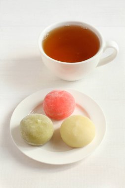 Üç çeşit Japon tatlı mochi - ballı nar, yeşil kibrit çayı, beyaz çay tabağında tutku meyvesi ve beyaz ahşap masada çay.