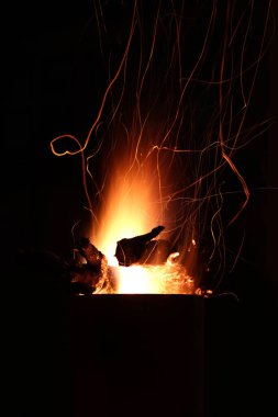 Ateş alevleri ve odun kıvılcımları gecenin karanlığında şöminenin dışında yanan metal bir şöminede karanlık gökyüzüne karşı.