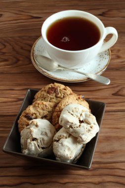 Ceviz ve kuru üzümlü yulaflı kurabiyeler, kare kasede fındıklı kremalı kurabiyeler ve ahşap masada bir fincan siyah çay. Yakın çekim.