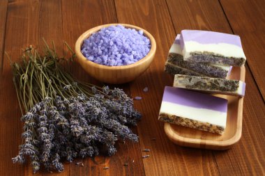 Bambu kasesinde lavantalı deniz tuzu, lavanta, bambu tabaktaki zeytin yağı ve kakao yağı sabunu ve kahverengi ahşap bir masada kurutulmuş lavanta çiçekleri bulunur. Yakın çekim..