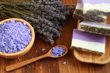 Bambu kasesinde lavantalı deniz tuzu, lavanta, bambu tabaktaki zeytin yağı ve kakao yağı sabunu ve kahverengi ahşap bir masada kurutulmuş lavanta çiçekleri bulunur. Yakın çekim..