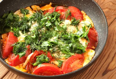 Domatesli çırpılmış yumurta, kahverengi ahşap bir masada doğranmış dereotu ve maydanoz serpiştirilmiş. Yakın çekim.