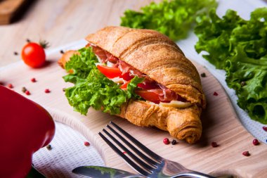 Ev yapımı kahvaltıda taze kruvasan, jambon, kırmızı biber ve peynirli sandviç, domates suyu ve ahşap masada bir fincan sıcak kahve..