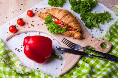 Ev yapımı kahvaltıda taze kruvasan, jambon, kırmızı biber ve peynirli sandviç, domates suyu ve ahşap masada bir fincan sıcak kahve..