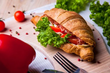 Ev yapımı kahvaltıda taze kruvasan, jambon, kırmızı biber ve peynirli sandviç, domates suyu ve ahşap masada bir fincan sıcak kahve..