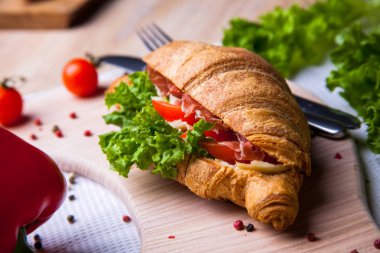 Ev yapımı kahvaltıda taze kruvasan, jambon, kırmızı biber ve peynirli sandviç, domates suyu ve ahşap masada bir fincan sıcak kahve..