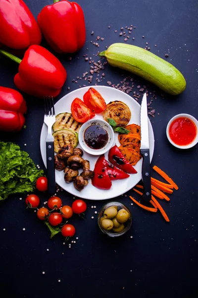 Veggy Suculentas verduras a la parrilla con una variedad de pimientos dulces, médula de bebé y tomate adornado con hierbas servidas en un plato con ingredientes visibles detrás — Foto de Stock