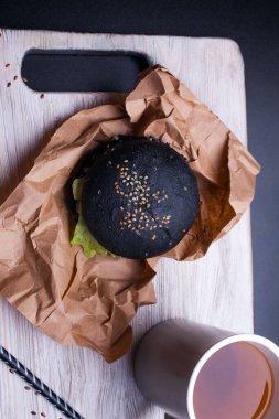Siyah susamlı siyah ekmek rulosu insan eli siyah arka planda bir kraft kağıdının üzerinde duruyor. Garip siyah hamburger ekmeğinin üstünde. Cadılar Bayramı yemeği