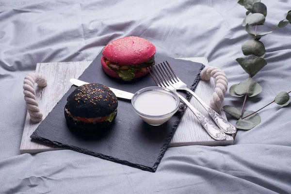 Colorful too mini burgers served on black plate as appetizer. Delicious classic, black and pink slider burgers loaded with beef patty, crispy chicken, lettuce, coleslaw, cheese, mushrooms. Image