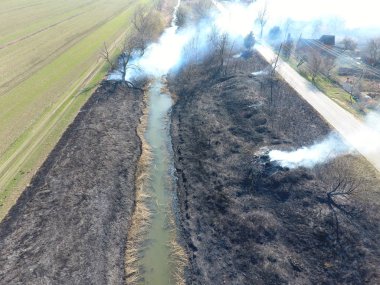 Sulama kanalı kuru ot yakma. Duman ve kuru ot alevi. Yanmış kuru ot