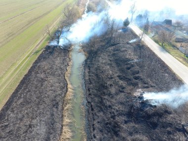 Sulama kanalı kuru ot yakma. Duman ve kuru ot alevi. Yanmış kuru ot
