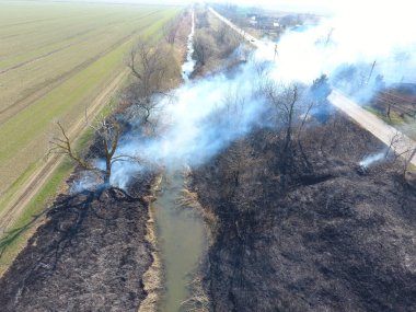 Sulama kanalı kuru ot yakma. Duman ve kuru ot alevi. Yanmış kuru ot