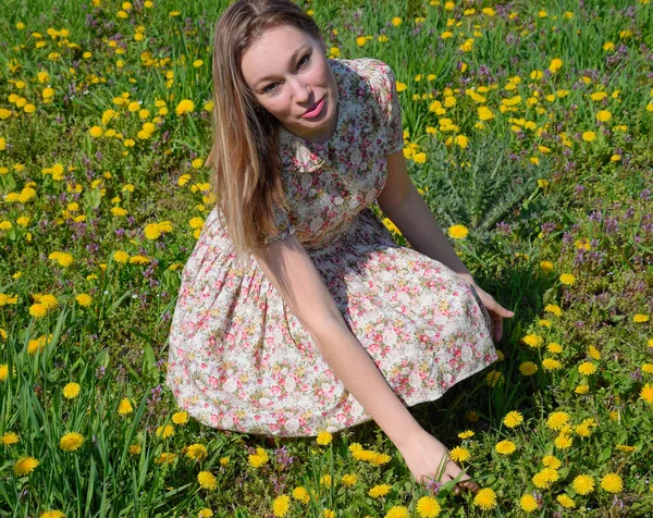 Uma menina em um vestido em uma clareira com dentes de leão. A menina entre as flores — Fotografia de Stock