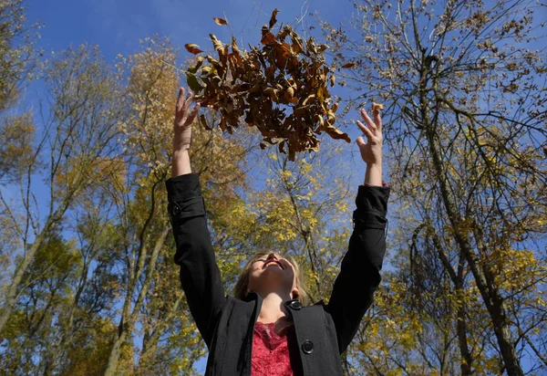 A woman throws up the autumn yellow leaves. Autumn in the park