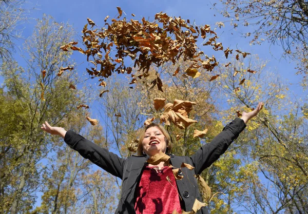 A woman throws up the autumn yellow leaves. Autumn in the park