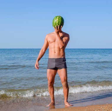 Sportif bir adam sahilde duran ve bütün bir karpuz tutarak. Bir adam elinde bir karpuz