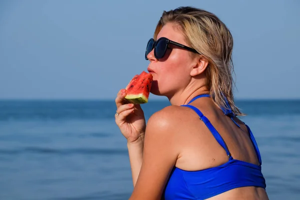 Блондинка в солнечных очках ест арбуз у моря. Сочный арбуз в руках женщины — стоковое фото