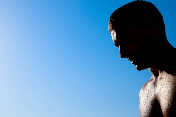 Silhouette d'un homme contre un ciel bleu et le soleil. Un homme dans des gouttes d'eau de mer — Photo