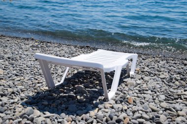 Kıyı şeridi tarafından taşlı bir plajda şezlong beyazdır. Denizin kenarında şezlong.