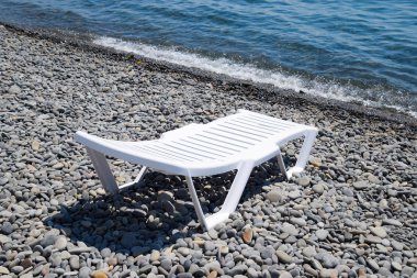Kıyı şeridi tarafından taşlı bir plajda şezlong beyazdır. Denizin kenarında şezlong.