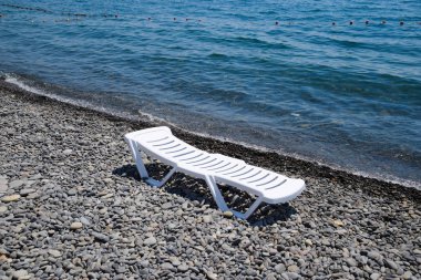 Kıyı şeridi tarafından taşlı bir plajda şezlong beyazdır. Denizin kenarında şezlong.