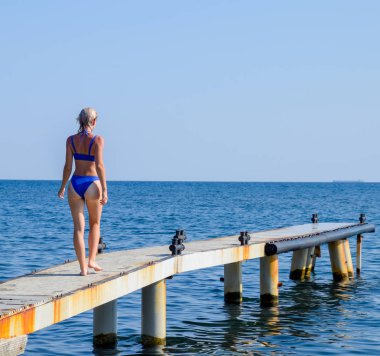 Mavi bikinili güzel bir kız iskele denize yürüyor. Deniz beton İskelesi. Suya rıhtımdan atlama. Güzel ganimet kızlar