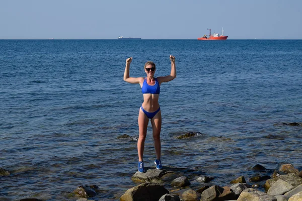 Una hermosa chica en bikini azul camina por el muelle hacia el mar. Muelle de concreto marino. Saltando al agua desde el muelle. Hermoso botín niñas —  Fotos de Stock
