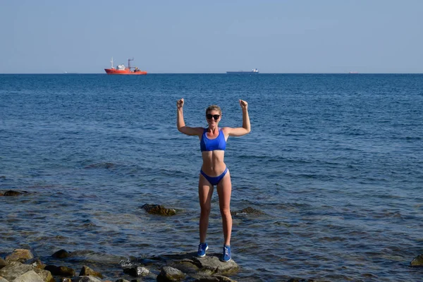 Una hermosa chica en bikini azul camina por el muelle hacia el mar. Muelle de concreto marino. Saltando al agua desde el muelle. Hermoso botín niñas —  Fotos de Stock
