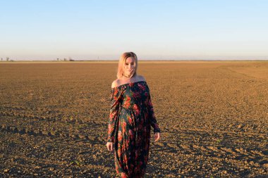 Gün batımı bir arka plan üzerinde kırmızı-siyah elbiseli sürülmüş bir alanda kadın.