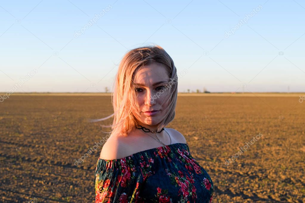 Woman in a plowed field in a red-black dress on a sunset background.