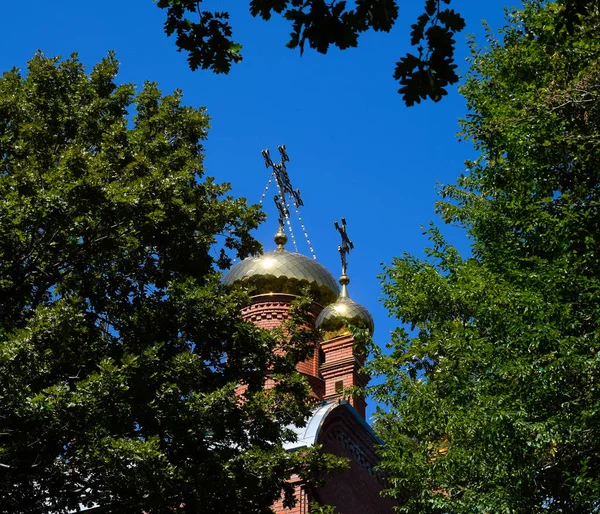 Cúpula da Igreja Ortodoxa com cruzes, vista através dos ramos de árvores contra o céu azul — Fotografia de Stock