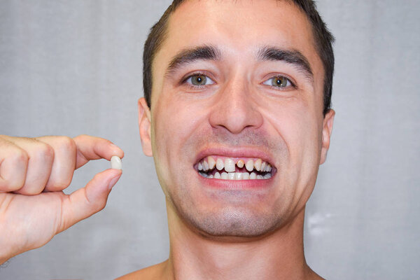 Dental prosthesis of metal ceramics in the hand of a man without a tooth. A patient without a tooth is trying on a denture. Tooth implantation, dental treatment.