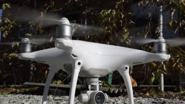 El drone phantom 4 de la compañía dji con hélices encendidas está parado sobre la grava . — Vídeo de stock