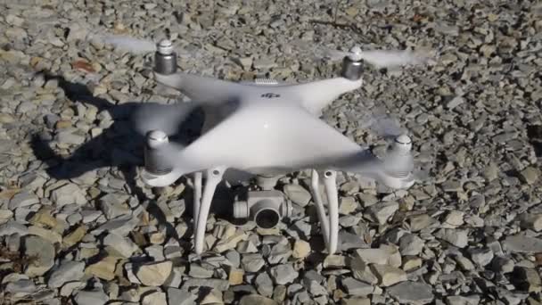 Drönare phantom 4 av det företaget dji med påslagen propellrar står på grus. — Stockvideo