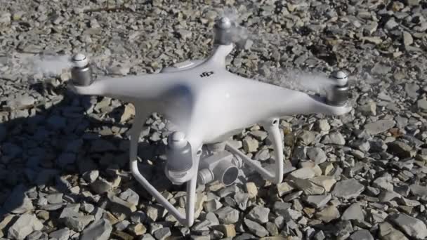 The drone phantom 4 of the company dji with turned on propellers is standing on the gravel. — Stock Video