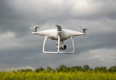 Krasnodar, Rusya Federasyonu - 30 Mayıs 2017: Beyaz dron çiçekli tecavüz alan üzerinde. Dron bulutlu gökyüzü karşı. Gökyüzünde helikopter uçuş.