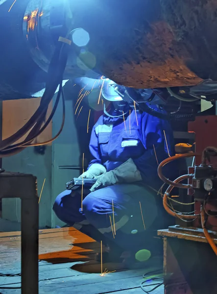 Welder resting during a break at work. Welding of the pipeline. Process of creation of welding connection by the special mobile machine. Worker sitting on a chair.