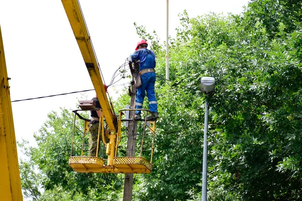 Electricistas reparan los cables en el poste con la ayuda de un elevador de grúa . — Foto de Stock