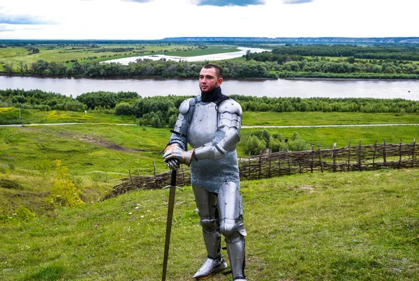 Рыцарь в доспехах стоит на фоне родных просторов, лесов и реки. Рыцарская броня и оружие — стоковое фото