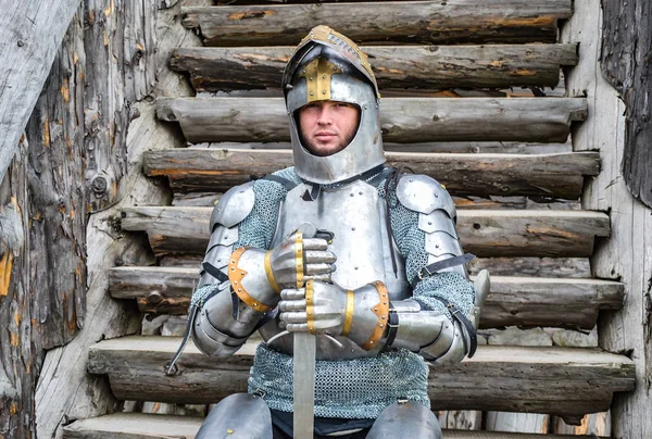 Knight in the armor on the wooden steps. Knightly armor and weapon