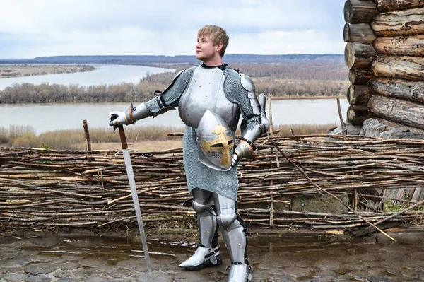 Chevalier en armure sur le fond d'une clôture en osier, d'une maison en bois et des étendues de la patrie . — Photo