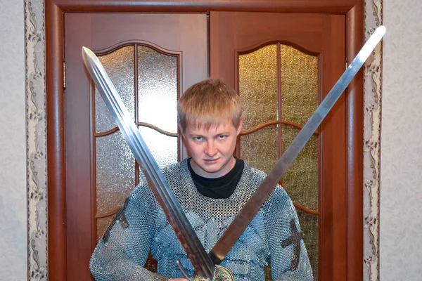 A man dressed up in a knights hauberk at home in his room. Knights sword in the hands of a man. — Stock Photo, Image