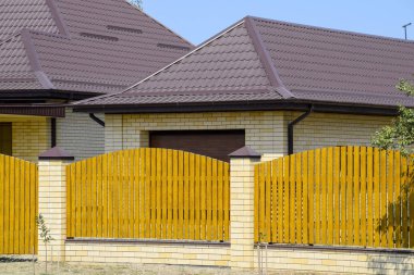 Oluklu metal profil çatısı ve ahşap çit tuğla ev. Güzel manzara cephe. Stil tasarım.