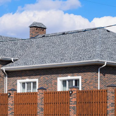 Asfalt shingle. Dekoratif bitüm Zona bir tuğla ev çatısında. Oluklu metal çit yapılmış