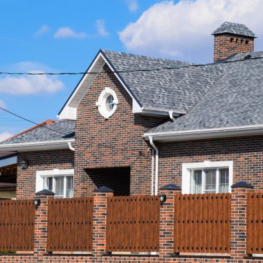 Asfalt shingle. Dekoratif bitüm Zona bir tuğla ev çatısında. Oluklu metal çit yapılmış