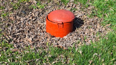 Çelik kapak, kırmızı renk. Park yerinde bir kanalizasyon var.